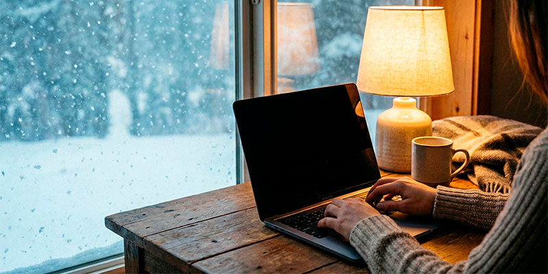 雪の降る窓辺と、暖かい室内でタイピングする手元